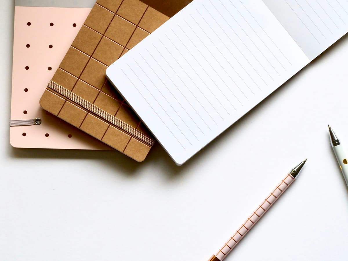 Trzy notesy obok siebie: w kropki, w kratkę i w linię, obok dwóch długopisów